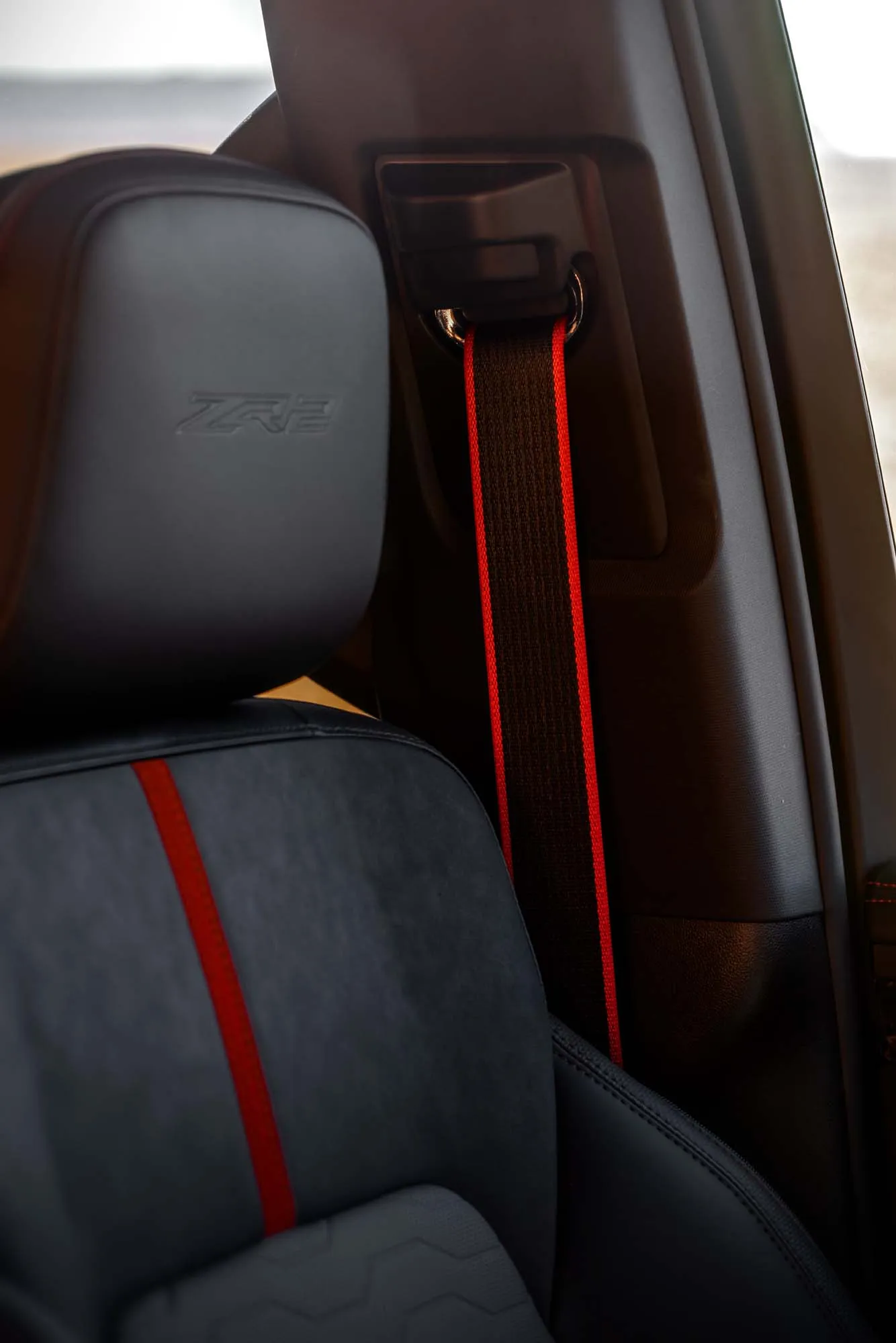 2027 Chevrolet Silverado 1500 ZR2 with Dark Galvinized Interior. Interior detail image focused on the front seat headrest, highlighting Torch Red detailing in the seat, Torch Red edged seatbelt and the debossed ZR2 logo headrest.